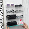 A hand displays a wall mounted acrylic display shelf featuring various pairs of eyeglasses and sunglasses.