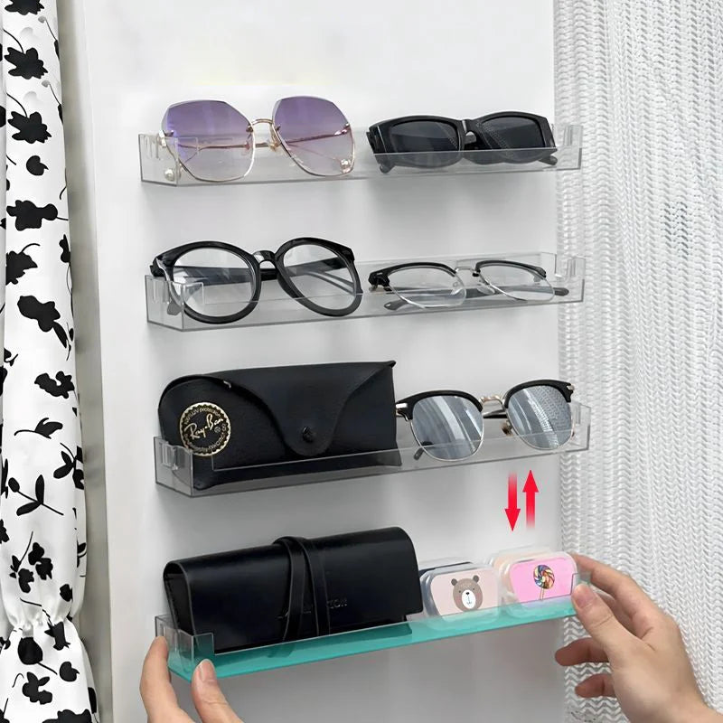 A hand displays a wall mounted acrylic display shelf featuring various pairs of eyeglasses and sunglasses.