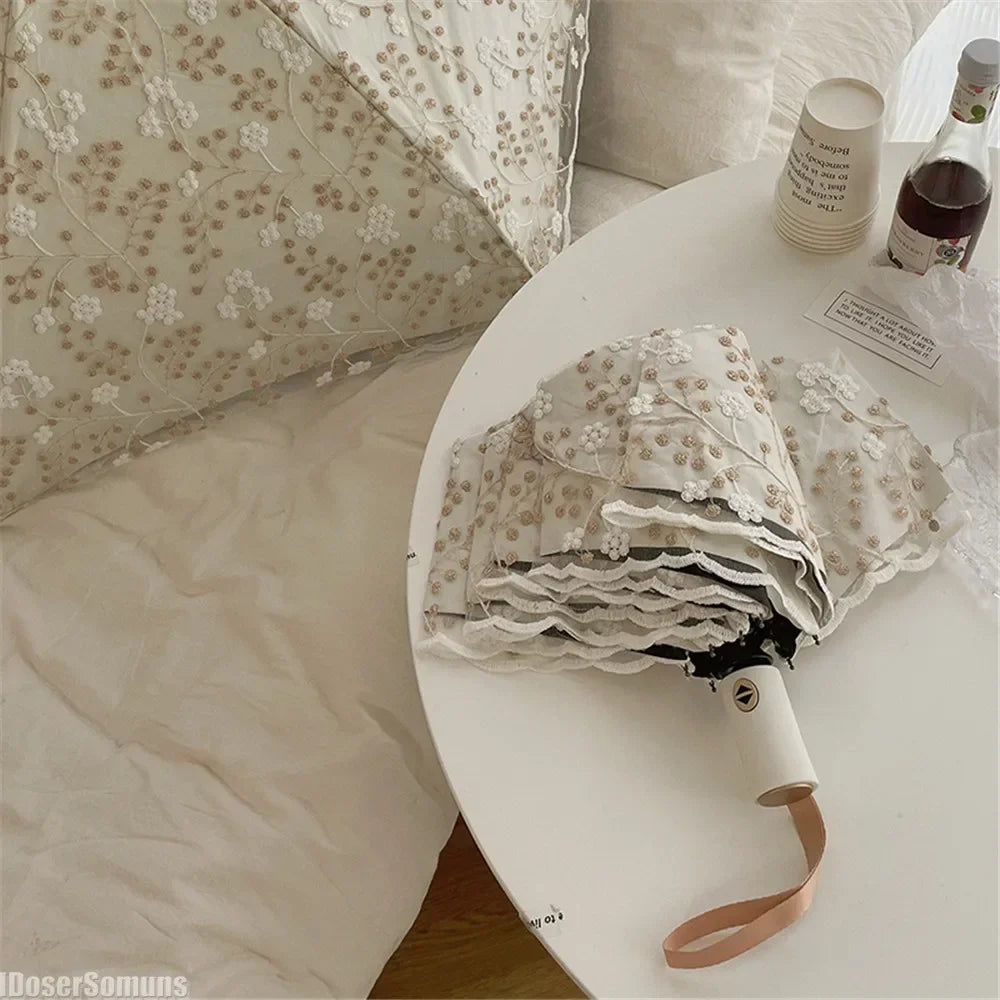 A white embroidered sun umbrella is displayed on a round white plate next to a pillow.
