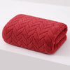 A deep coral red velvet bath towel with a textured diamond pattern rolled up.