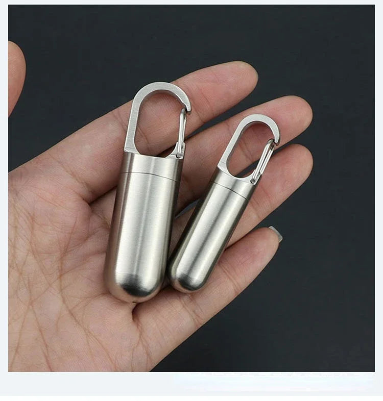 A hand holds a stainless steel travel pill box and first aid container with hinged lids.