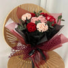 Un bouquet de cœurs de coton faits main, roses et rouges, emballés dans du papier foncé et attachés avec un ruban de dentelle