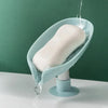 A leaf-shaped suction cup soap holder with a self-draining tray is shown, dripping water onto a white surface.