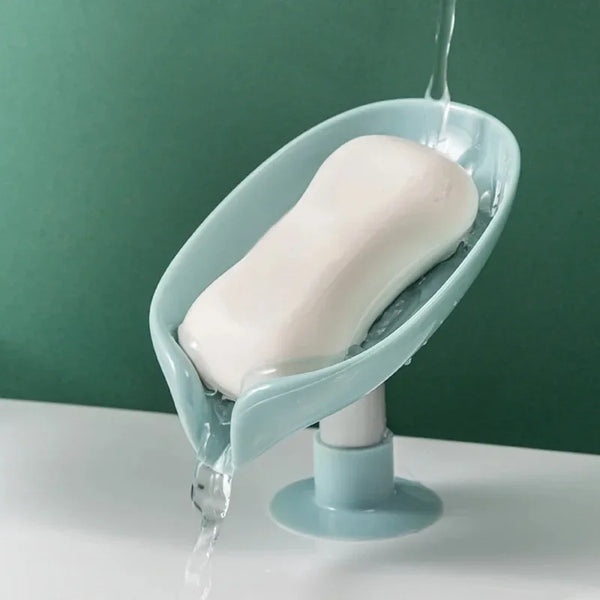 A leaf-shaped suction cup soap holder with a self-draining tray is shown, dripping water onto a white surface.