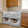 Silver Oxford washing machine cover with roll edge displayed next to a wooden cabinet.