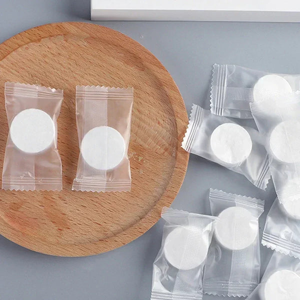 Several packets of portable compressed face and hand wipes are displayed on a wooden board.