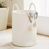 A large white woven storage hamper with handles sits on a light rug next to a window.