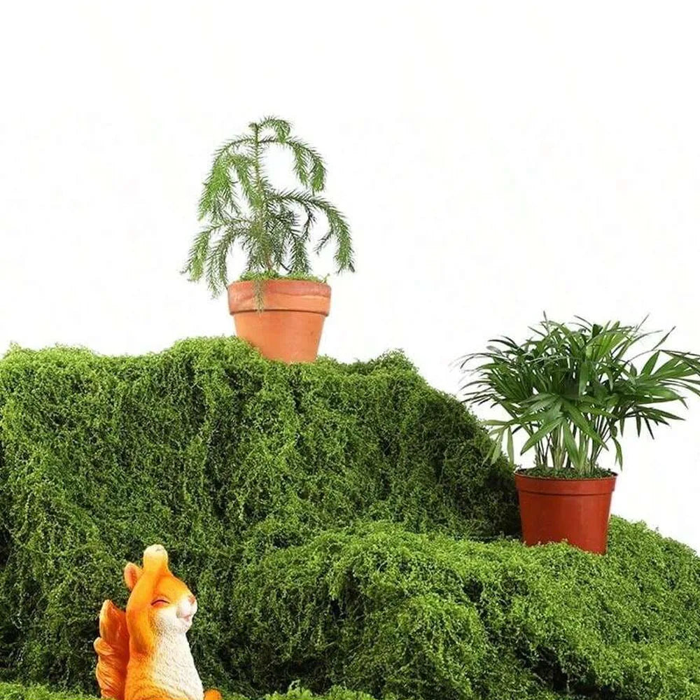 An artificial moss garland is displayed on a green textured surface with a small potted plant and a small orange squirrel.