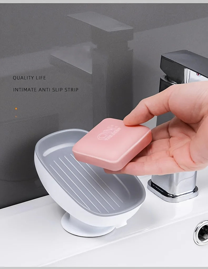 A hand is placing a pink leaf-shaped anti-slip strip onto a white bathroom soap dish drainer.