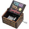 A vintage engraved wooden music box with a lid featuring the text YOU ARE my sunshine and a silver key.