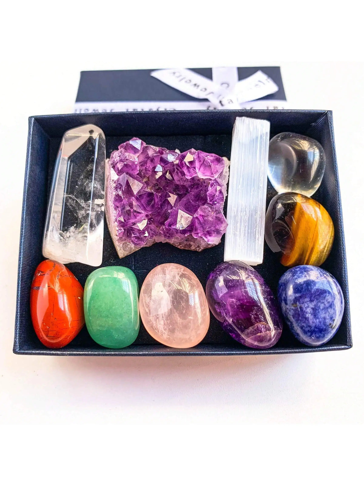 A set of natural crystals including amethyst, quartz, citrine, and other stones displayed in a black box.