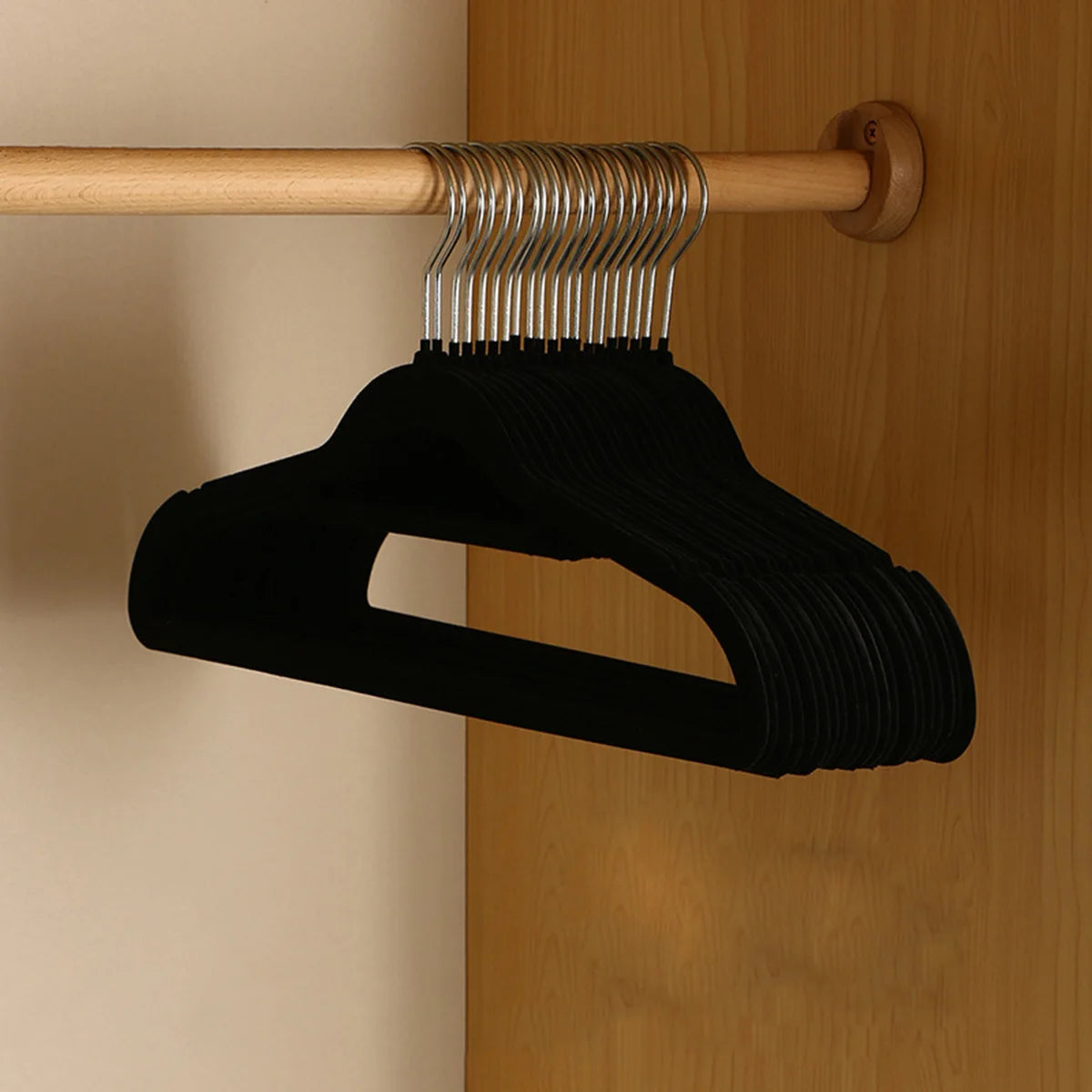 A black velvet slim hanger set with metal pegs hanging from a wooden rod on a cabinet door.