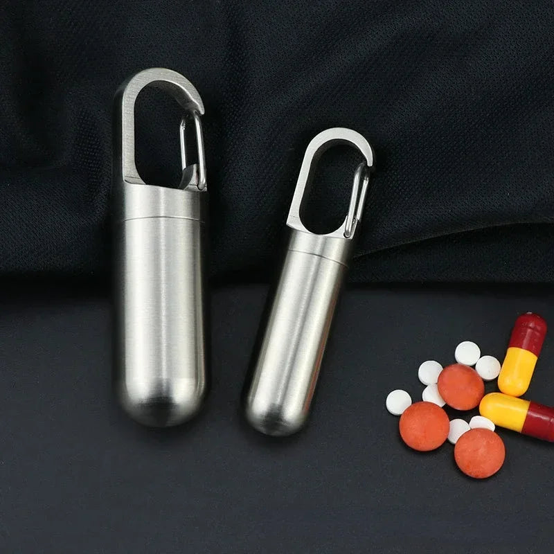 Two stainless steel travel pill box and first aid containers resting on a dark surface.