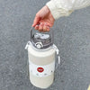 A hand is holding a large white insulated tumbler with a stainless steel lid and handle against a gray asphalt background.