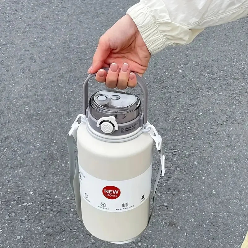 A hand is holding a large white insulated tumbler with a stainless steel lid and handle against a gray asphalt background.