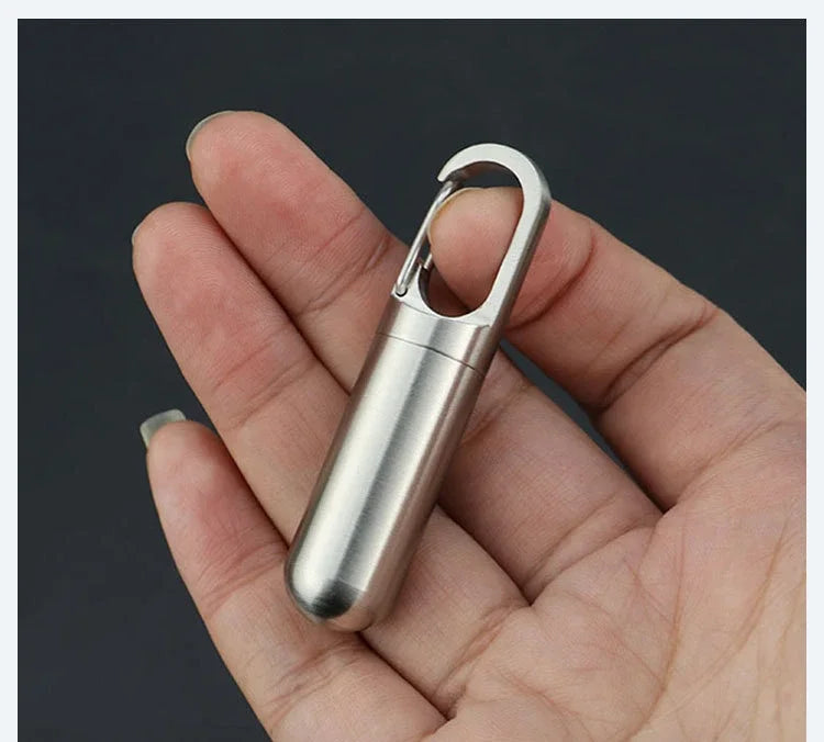 A hand holds a stainless steel travel pill box and first aid container.