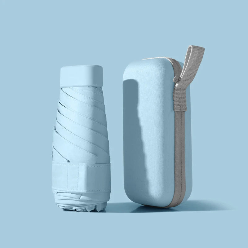 A light blue compact 5-fold travel umbrella with a gray strap is shown against a pale blue background.
