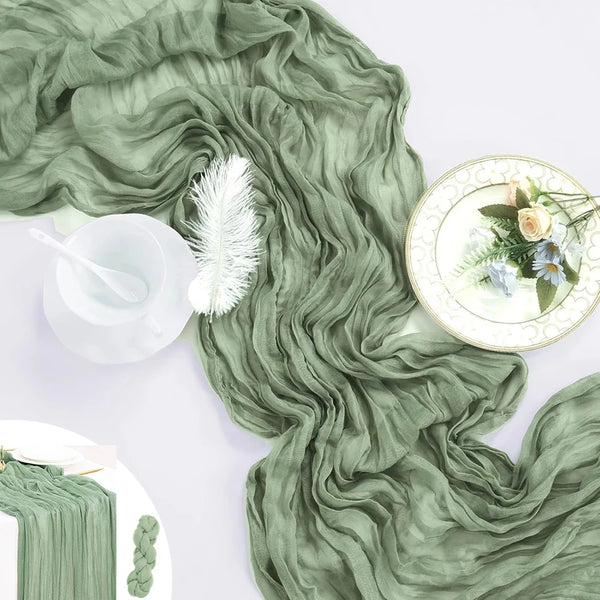 A flowing sage green sheer fabric draped across a white surface with a glass, feather, and plate.