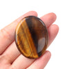 A polished, oval-shaped natural quartz thumb stone with swirling brown and amber patterns held in a hand.