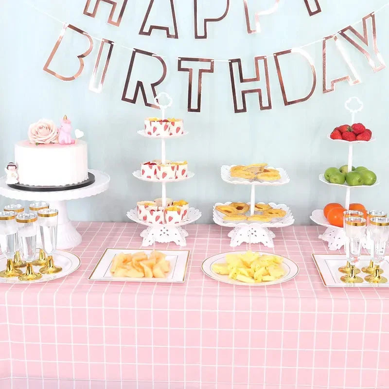 A pink birthday party table decorated with a banner, tiered cakes, and various fruits and candies on stands.