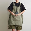 A woman wearing a olive green waterproof outdoor work apron over a black shirt and khaki shorts.