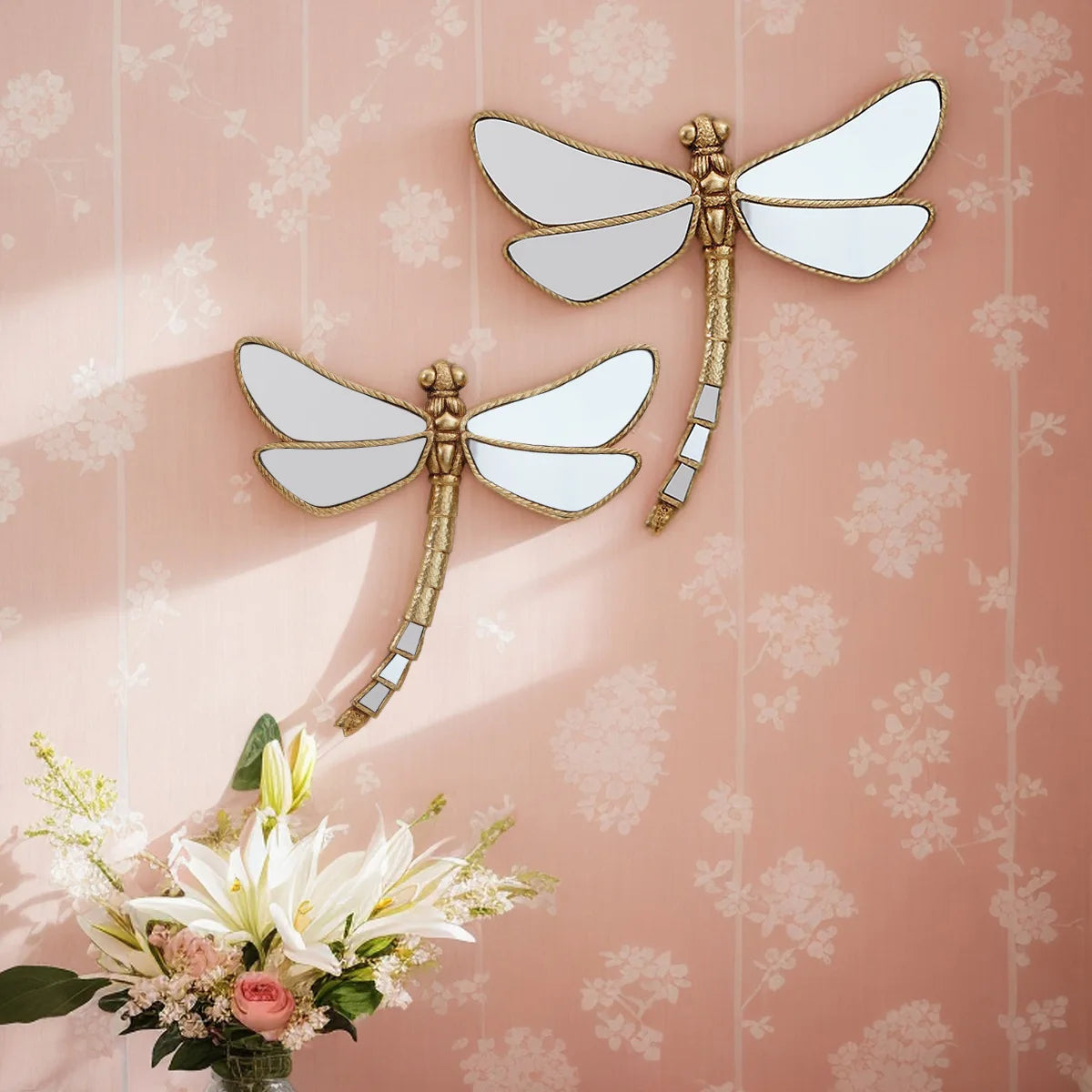 Golden dragonfly mirror wall decor featuring white wings and gold accents against a pink floral background.