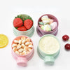 A collection of colorful silicone food storage boxes filled with various baby snacks like strawberries and fruit pieces.
