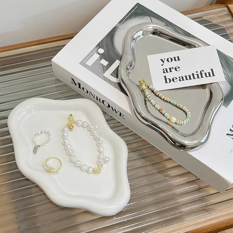 A silver jewelry organizer tray with a necklace and earrings is displayed on a white tray and next to its packaging.