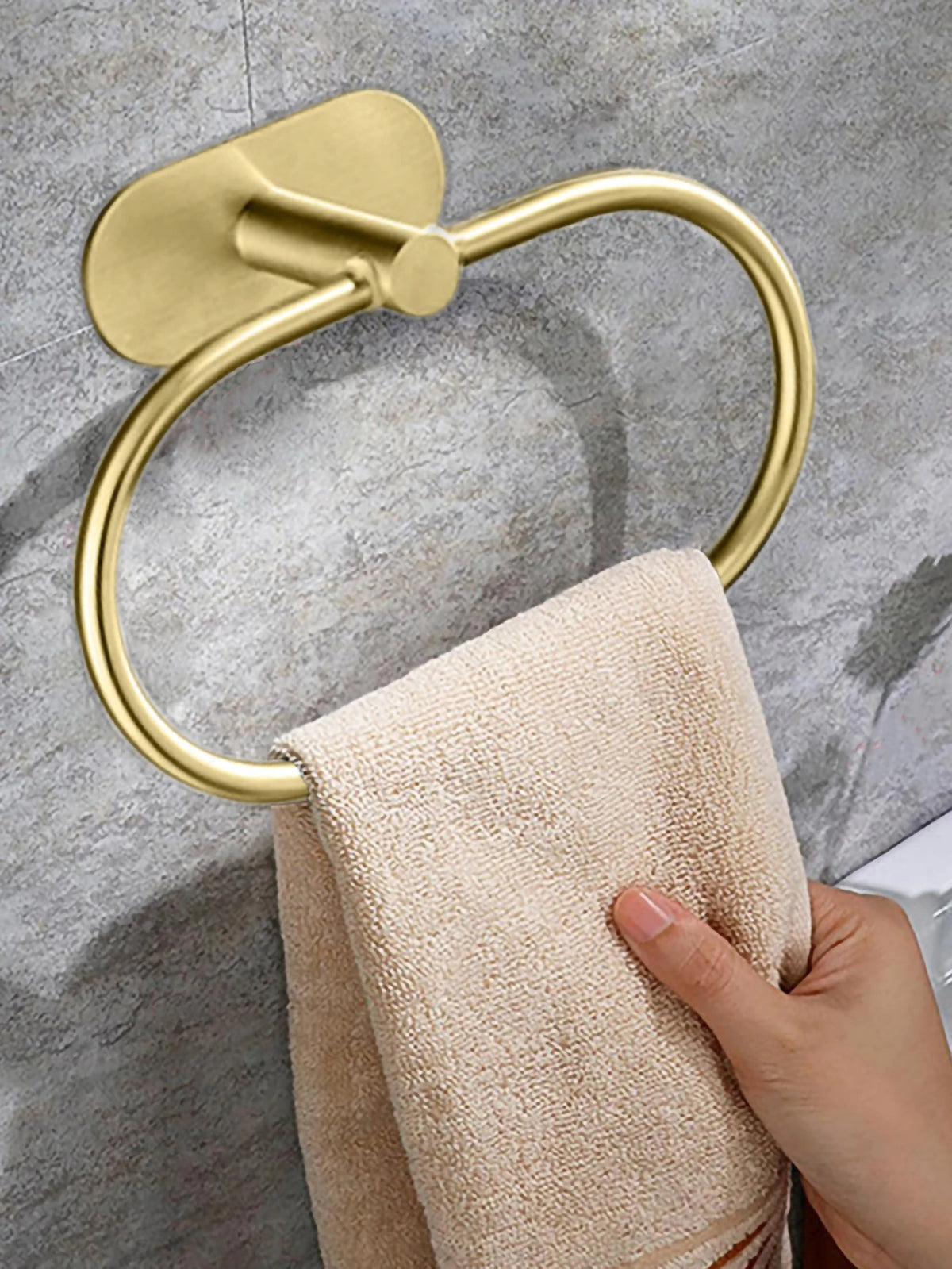 Un toallero adhesivo de acero inoxidable y latón sostiene una toalla beige contra una pared de azulejos grises.