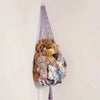 Macrame stuffed animal storage hammock filled with various soft toys hanging on a white wall