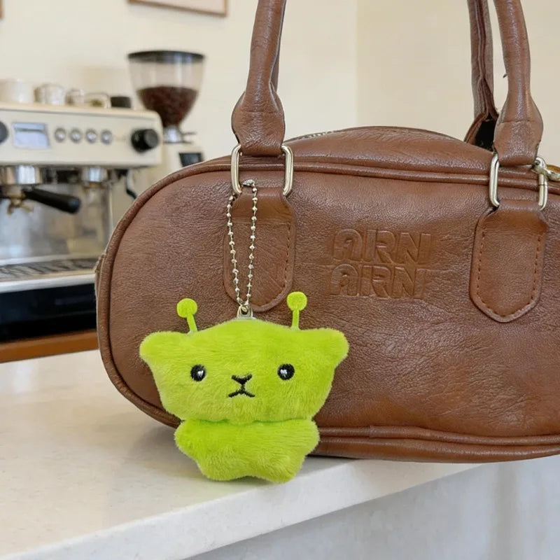 A bright lime green plush cat keychain is displayed resting on a brown leather handbag.