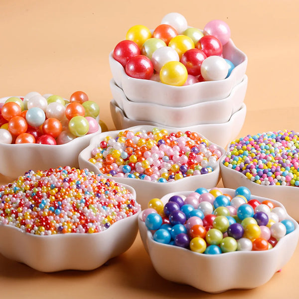 A collection of colorful pearl ball cake decoration sprinkles in various shades and arranged in white bowls.