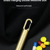 A brass hanging buckle medicine box with a gold-toned clasp and several pills on a black background.