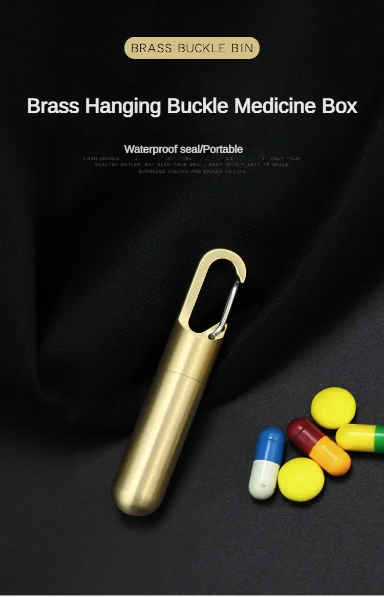 A brass hanging buckle medicine box with a gold-toned clasp and several pills on a black background.