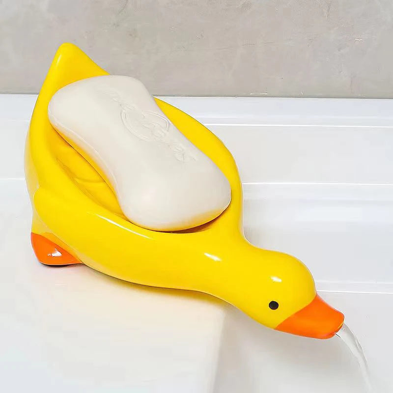 A yellow duck-shaped soap dish with a white bar of soap is shown on a white surface.