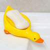 A yellow duck-shaped soap dish with a white bar of soap is shown on a white surface.
