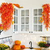 Artificial flower garland in shades of orange and yellow decorating a white wall with glass-paned cabinets.