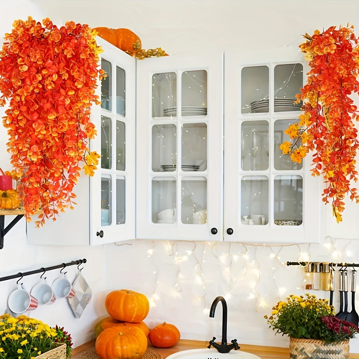 Artificial flower garland in shades of orange and yellow decorating a white wall with glass-paned cabinets.