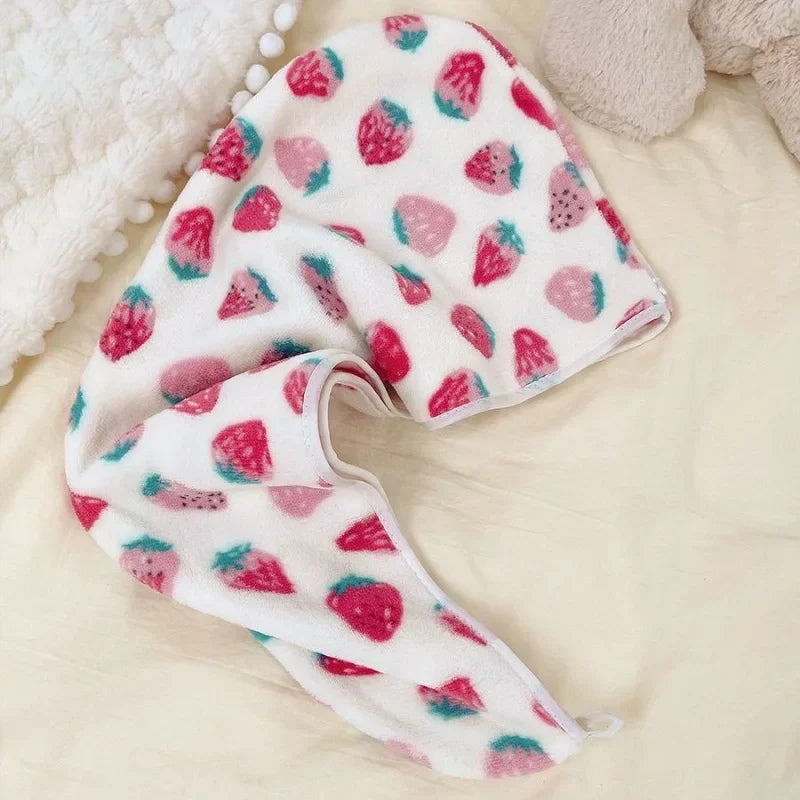 A pink and white strawberry print quick-drying hair towel headscarf lying on a light beige surface.