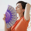 A woman holds and opens a purple and gold patterned handheld folding fan.