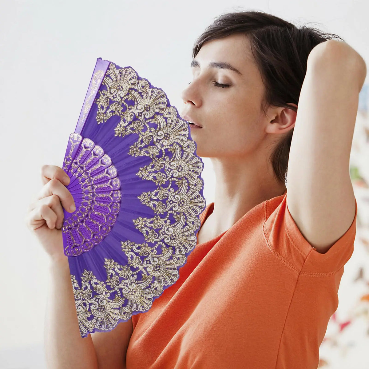 A woman holds and opens a purple and gold patterned handheld folding fan.