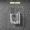 A clear, square adhesive wall hook is shown wet on a dark surface surrounded by water droplets.
