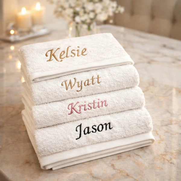 A stack of white cotton face towels with names embroidered on them: Kelsie, Wyatt, Kristin, and Jason.