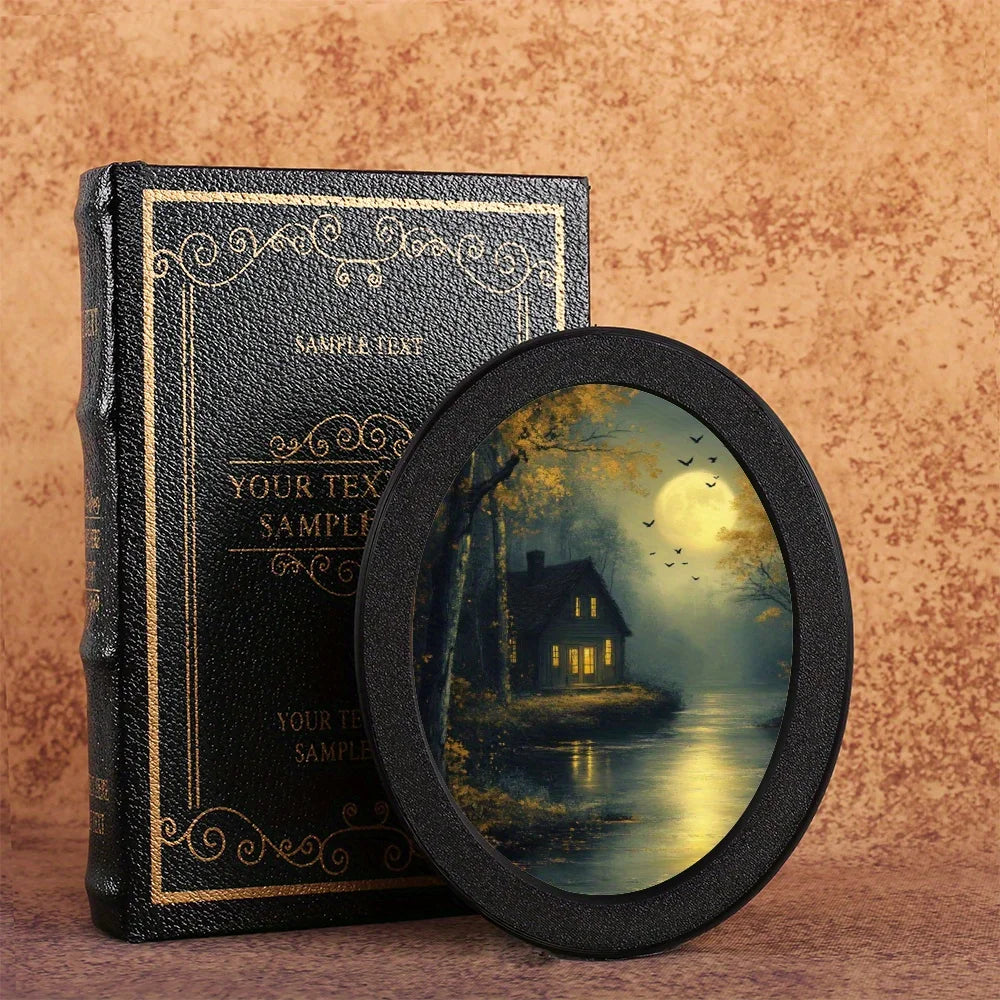 A black leather-bound box with gold lettering next to a round photo frame featuring a moonlit landscape.