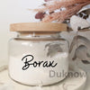A clear glass jar filled with white borax powder, resting on a light surface.