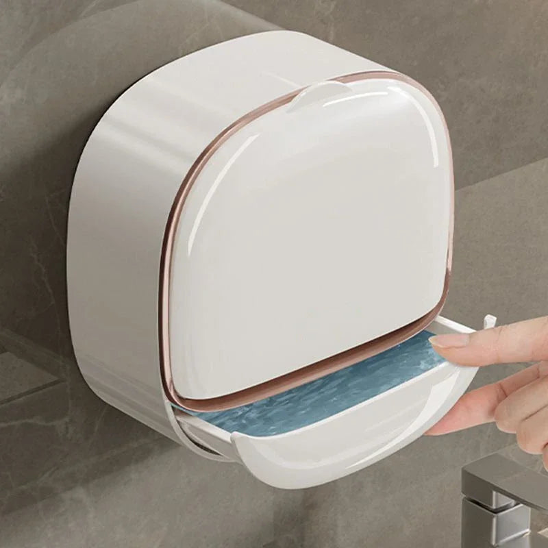 A white wall-mounted soap dish with a lid is shown being opened by a hand.