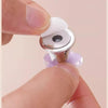 A hand is pressing a flower-shaped toilet flush button with a silver and white mechanism.