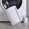 A white mesh shoe cleaning bag is shown next to a washing machine drum.
