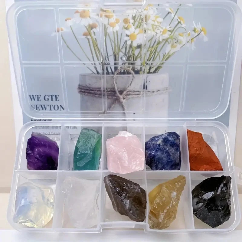 A clear plastic box containing various natural crystal stones including purple, green, pink, blue, and orange specimens.