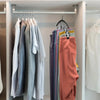 A row of clothing hangers displaying various colored shirts and sweaters in a closet organizer.